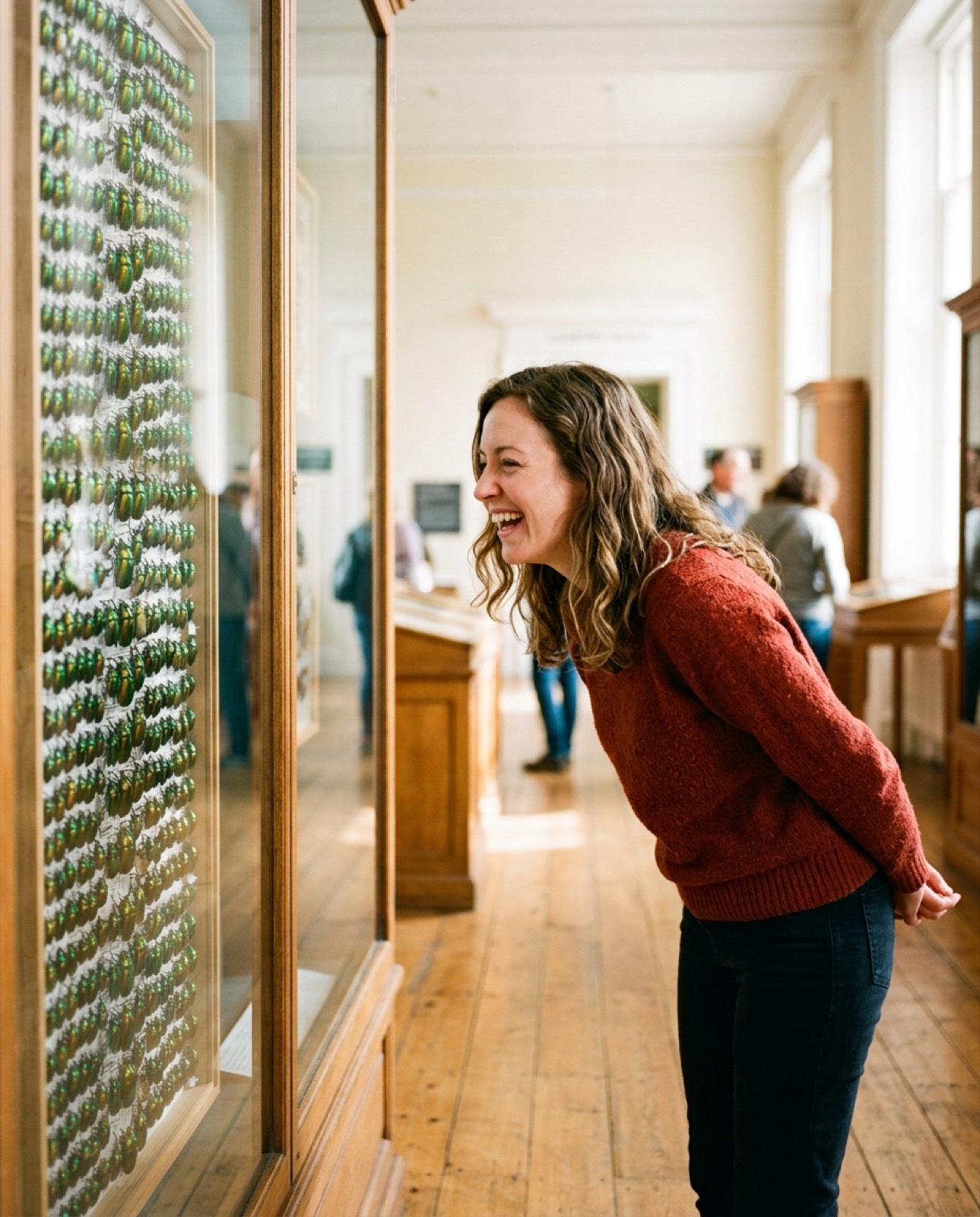A woman bends towards a tall case of pinned beetles, laughing.